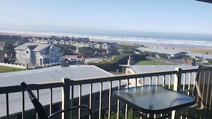 A balcony with a table and chairs overlooking a residential area with houses and a beach. - Gearhart House G670 (Gearhart)