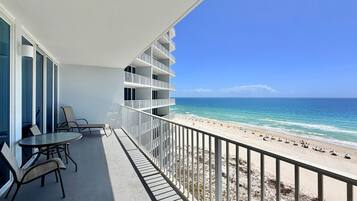 A balcony with a view of the beach, outdoor seating, and a railing.