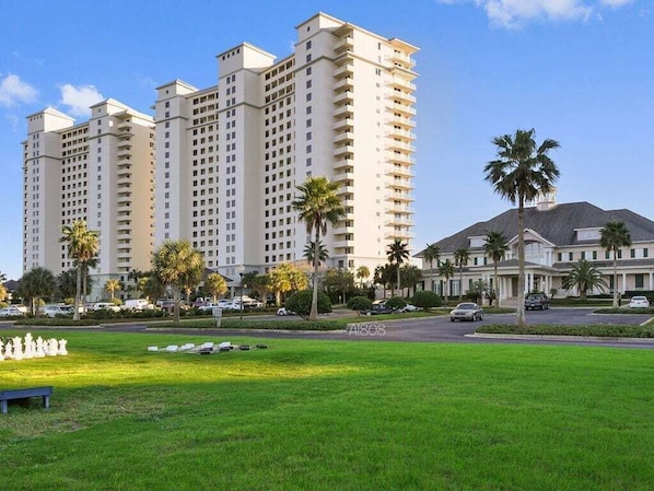 A high-rise hotel with multiple floors, a well-maintained lawn, and palm trees.