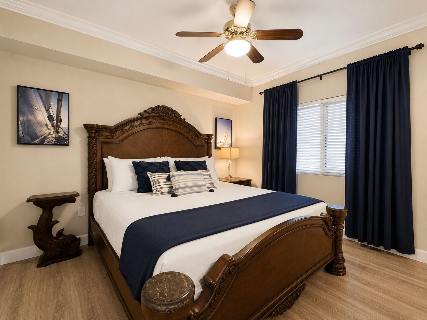 Une chambre à coucher avec un lit en bois, un ventilateur de plafond, une fenêtre avec des rideaux et des œuvres d’art accrochées aux murs.