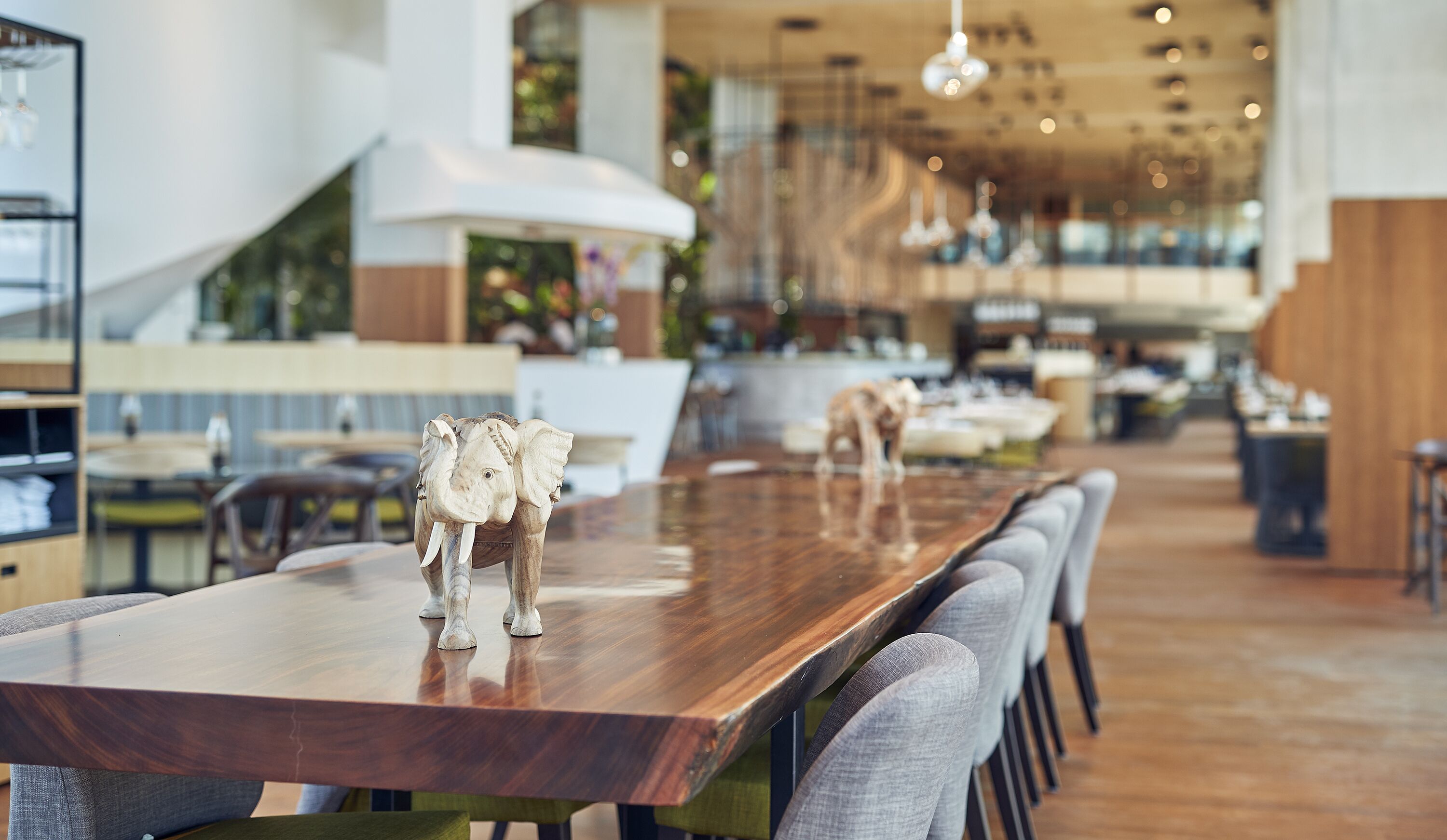 Un restaurante moderno con una larga mesa de madera, sillas tapizadas en gris y lámparas colgantes.