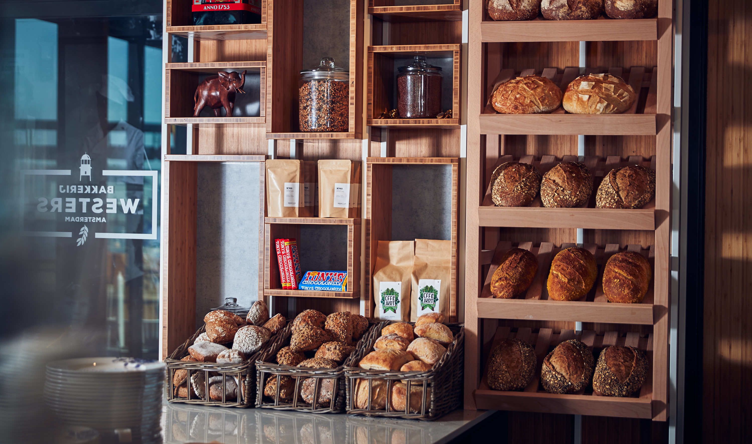 A bakery display with various breads and pastries, wooden shelves, and a window with a sign.