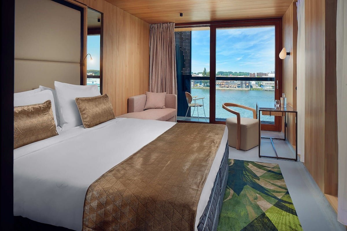 Une chambre d’hôtel avec un grand lit, un bureau, une chaise et une vue sur une rivière et des bâtiments.
