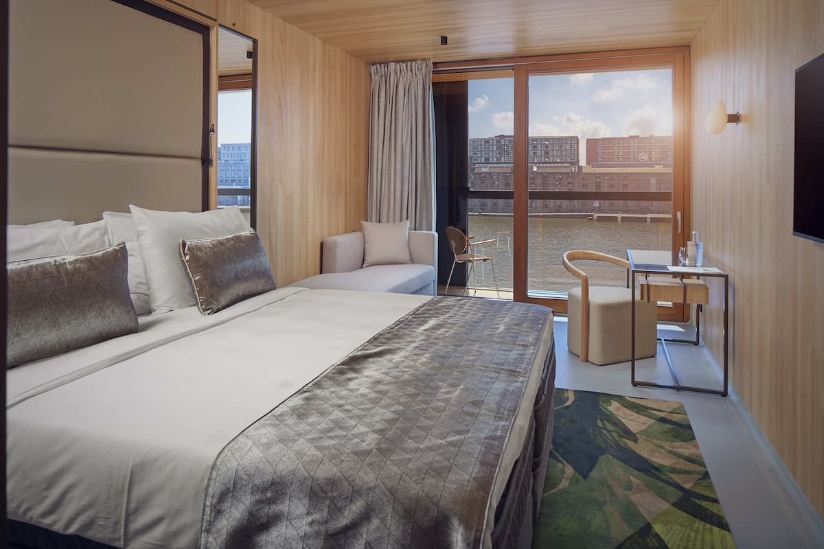 Une chambre d’hôtel avec un grand lit, un bureau, une chaise et une vue sur la ville par la fenêtre.