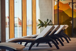 Une rangée de chaises longues dotées de pieds noirs incurvés, disposées devant une grande fenêtre offrant une vue sur une chaîne de montagnes.