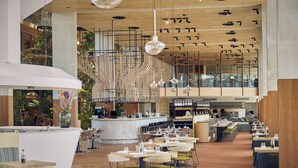 Amplio espacio interior con varias mesas y sillas para comer, una barra central y una escalera que conduce a un nivel superior.