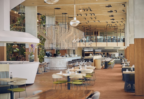 A spacious indoor area with multiple dining tables and chairs, a central bar area, and a staircase leading to an upper level.