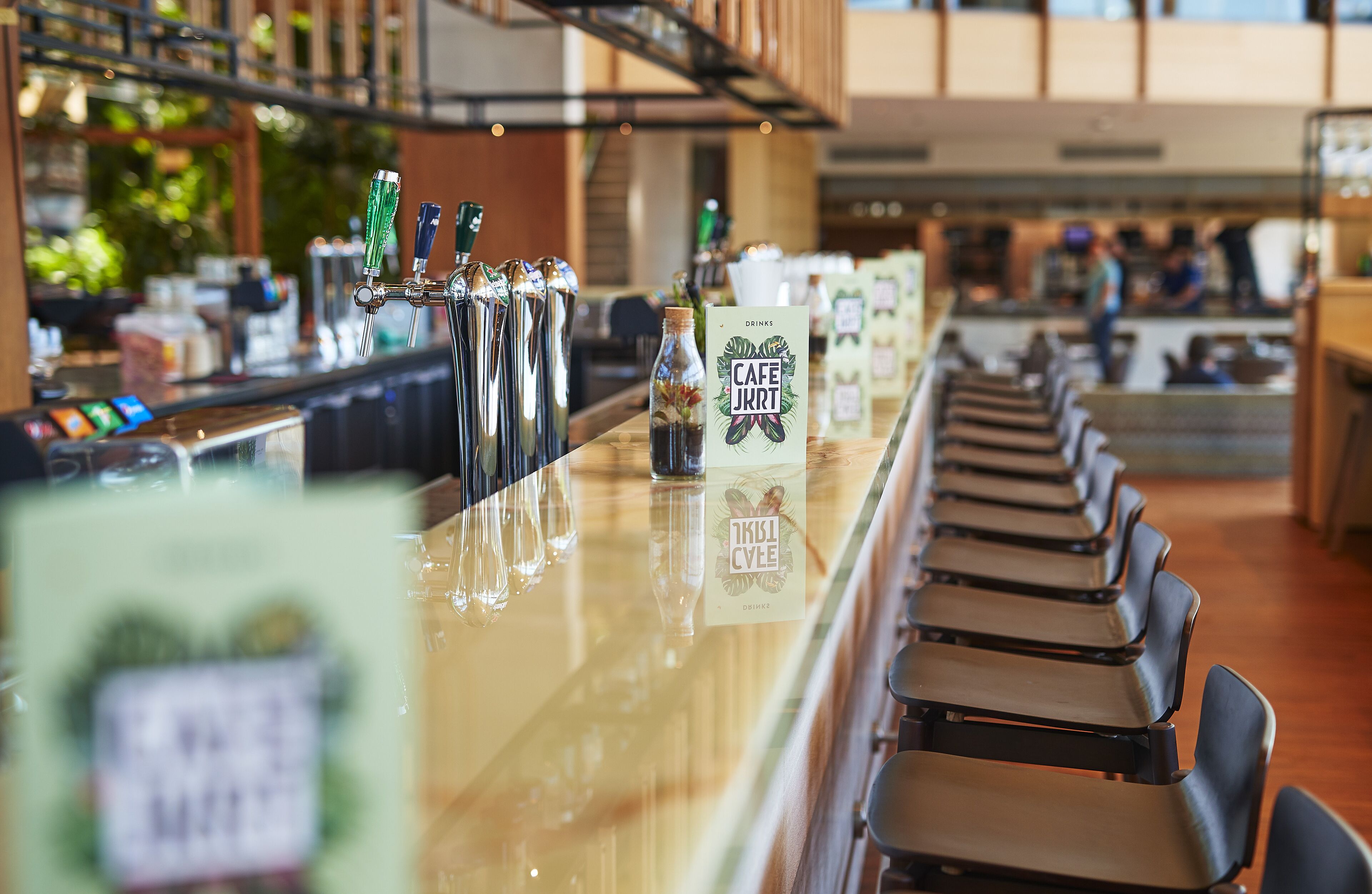 Een bar met verschillende bierkraan aansluitingen, een fles 'Cafe JKRT' drank en een menukaart standaard.