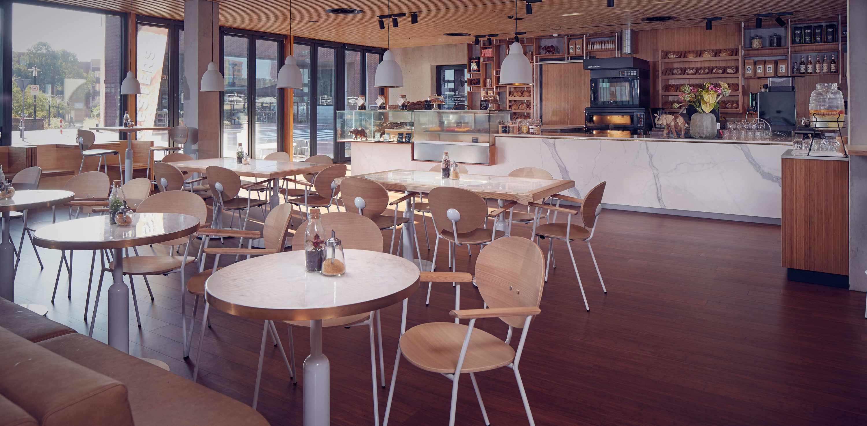 A modern cafe with round tables and chairs, a kitchen area, and large windows.