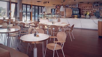 A modern cafe with round tables and chairs, a kitchen area, and large windows.