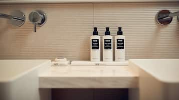Un baño con encimera de mármol, tres botellas de productos FAYR Cosmetics y un jabonera.
