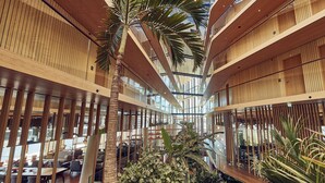 Un atrio moderno con paneles de madera, barandas de vidrio y plantas de interior.