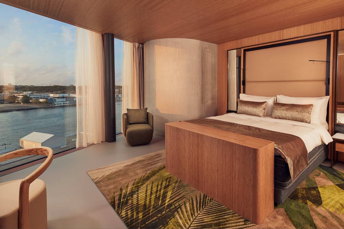 Une chambre moderne avec un grand lit, une chaise, une table de chevet et une vue sur un plan d’eau.