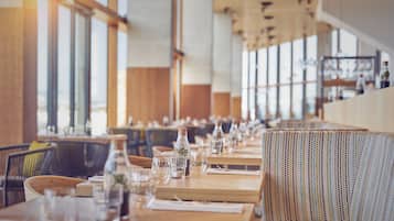 Een restaurant met houten tafels en stoelen, grote ramen en een lange toonbank.
