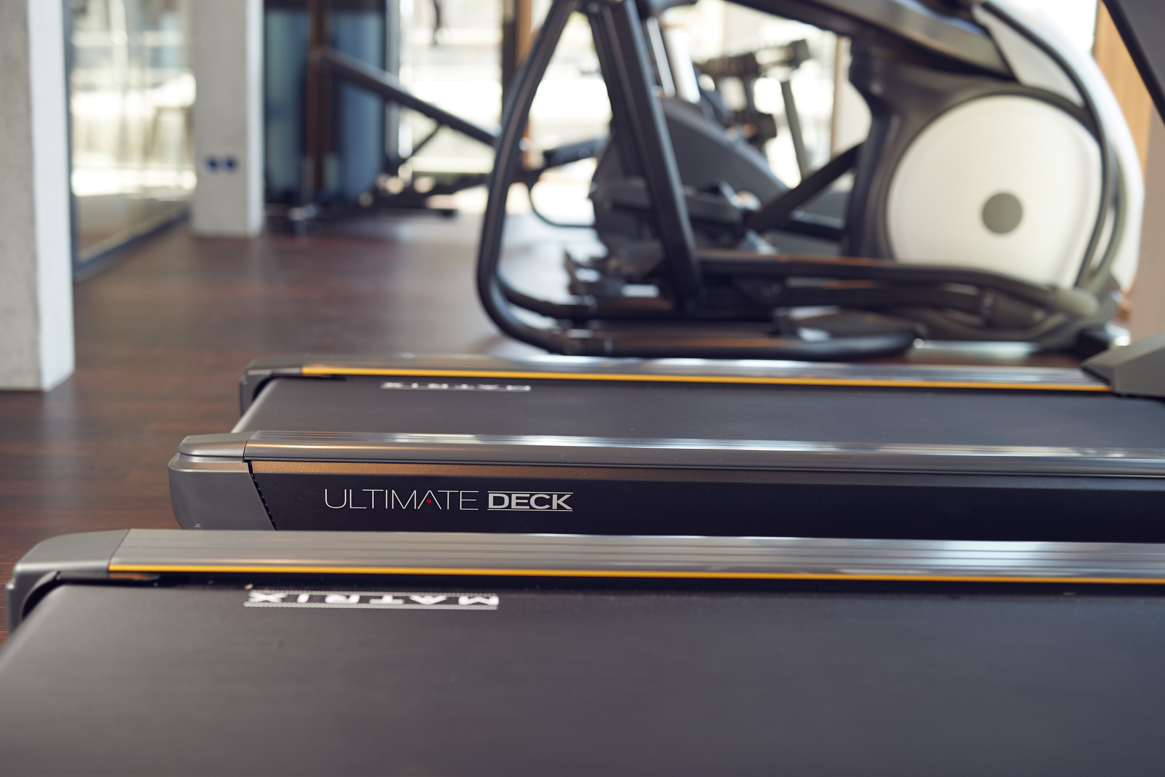 A treadmill with the label "ULTIMATE DECK" in a gym setting.