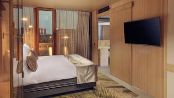 Una habitación de hotel moderna con una cama, un televisor de pantalla plana y vistas a la ciudad a través de amplias ventanas.