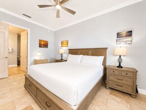 A bedroom with a large bed, two bedside tables with lamps, a ceiling fan, and artwork on the walls.