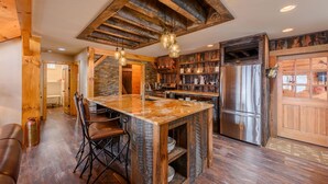 A rustic kitchen with a central island, wooden beams, and a stainless steel refrigerator. - Luxury Mountain Cabin with Views (Banner Elk)