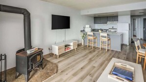 Una sala de estar moderna con chimenea, un televisor de pantalla plana y una zona de cocina con taburetes de bar.
