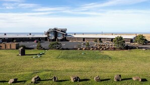 A building with a flat roof, a parking lot, and a grassy area with rocks.