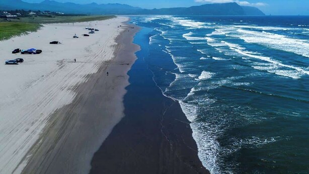 A beach with a long stretch of sand, waves crashing onto the shore, and a clear sky.