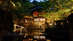 A traditional Japanese garden with a wooden pavilion, a stone lantern, and a pond reflecting the structures. - Kamei no Yu (Yamanouchi)