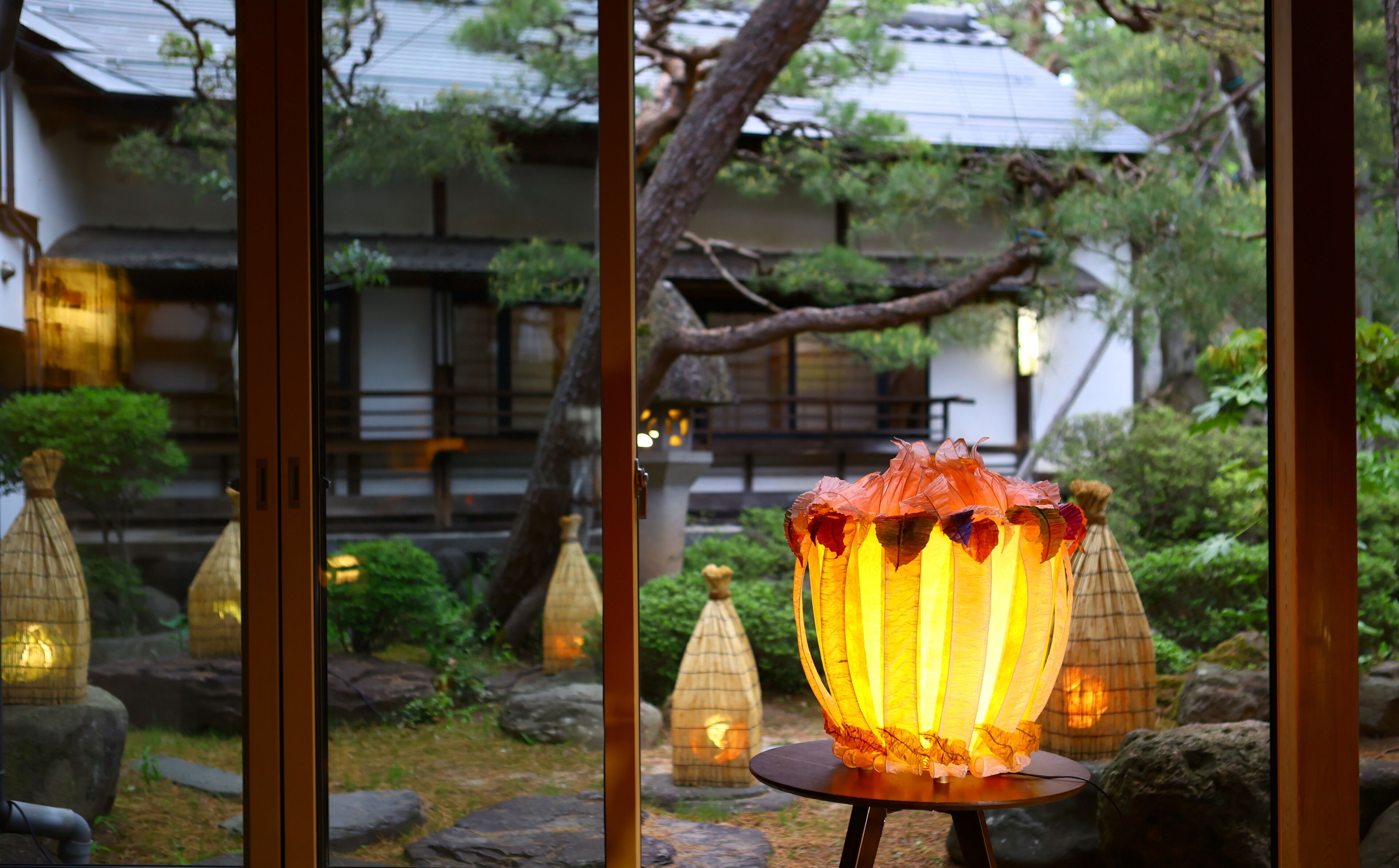 A traditional Japanese lantern in a garden with stone paths and a wooden building in the background.