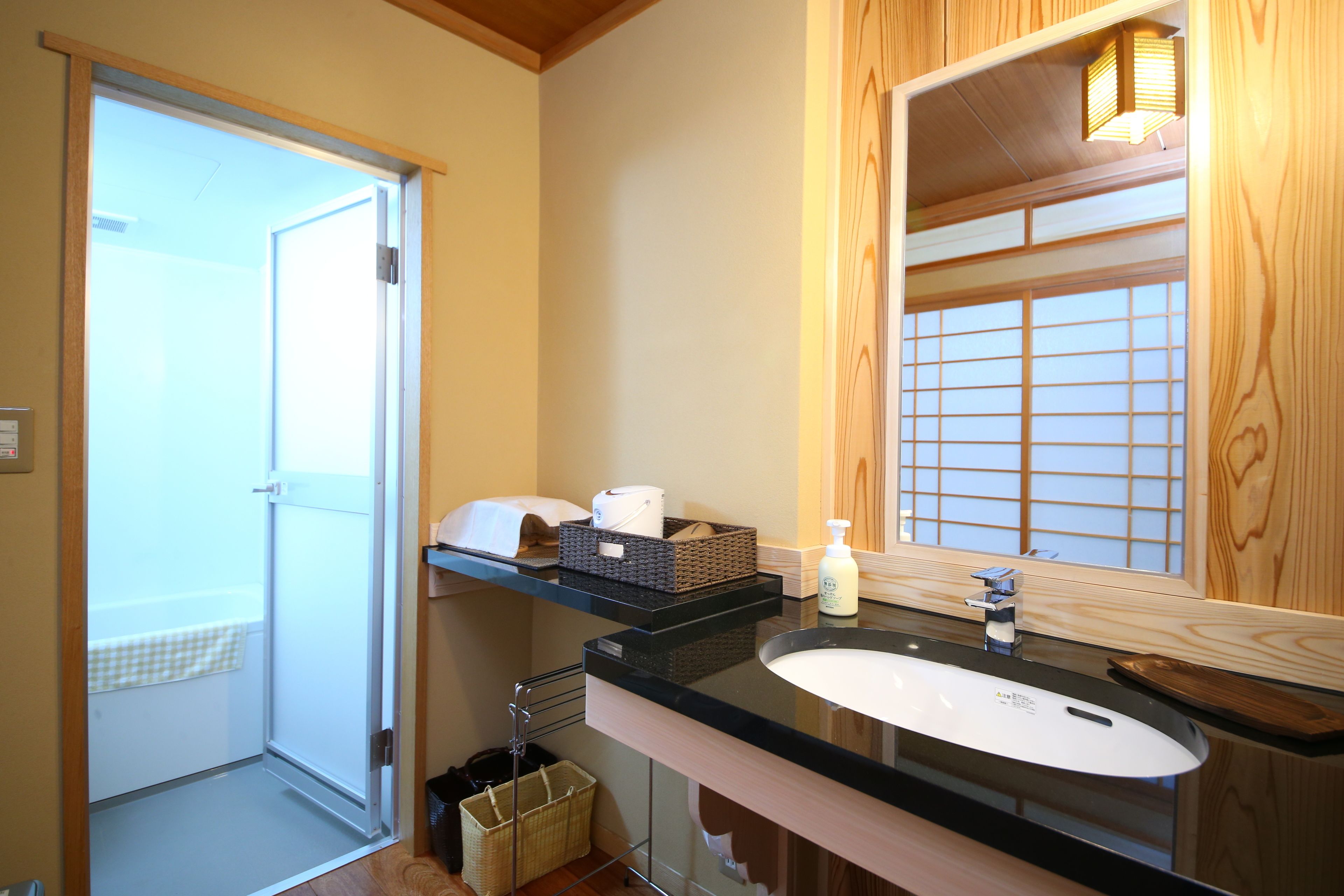 A modern bathroom with a glass door leading to a balcony, a black countertop, a white sink, and a wooden vanity.