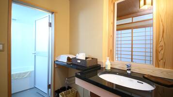 A modern bathroom with a glass door leading to a balcony, a black countertop, a white sink, and a wooden vanity.
