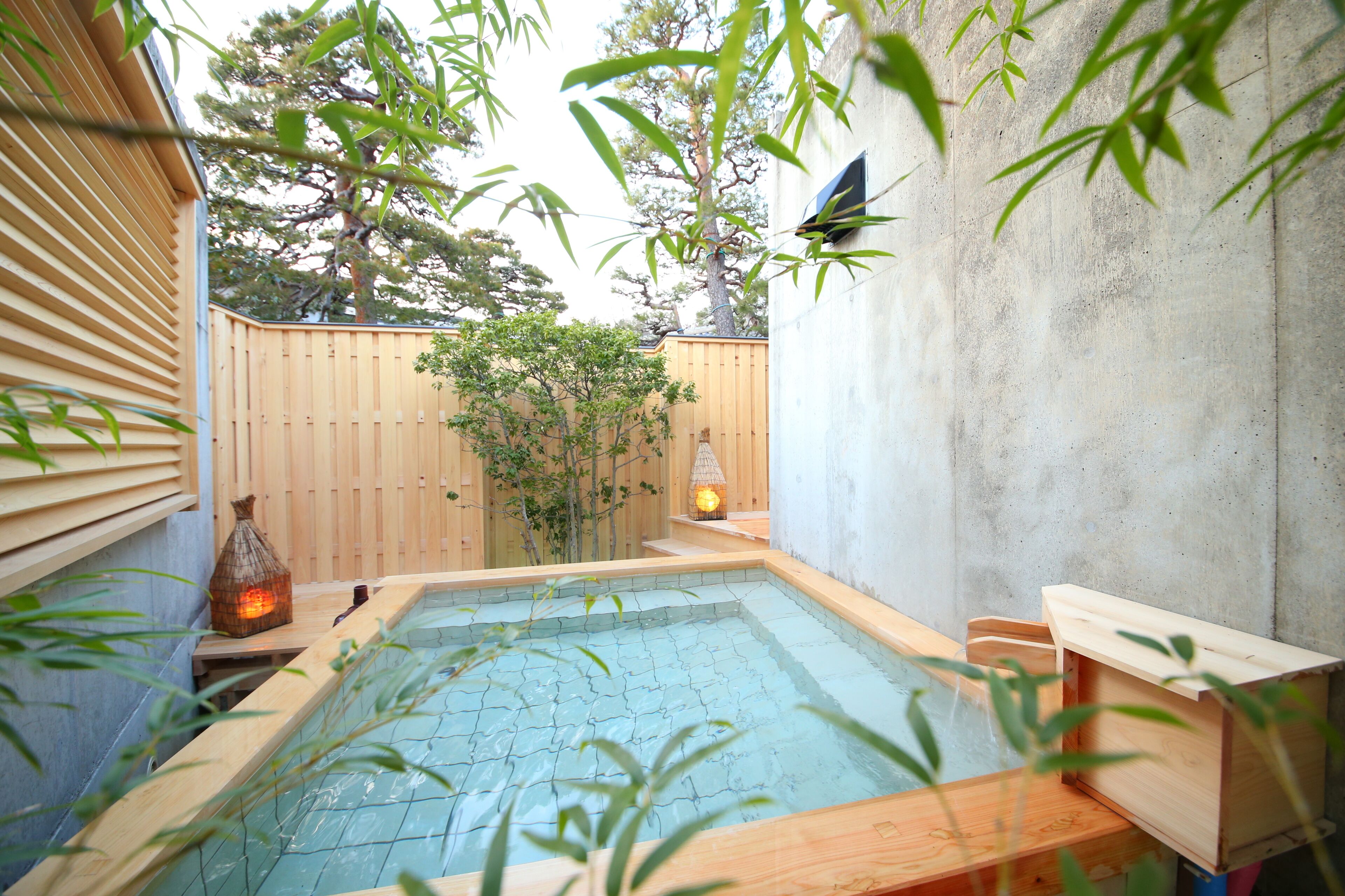 Ein kleines, überdachtes Whirlpool mit Holzterrasse, umgeben von Bambuspflanzen und einem Holzzaun.