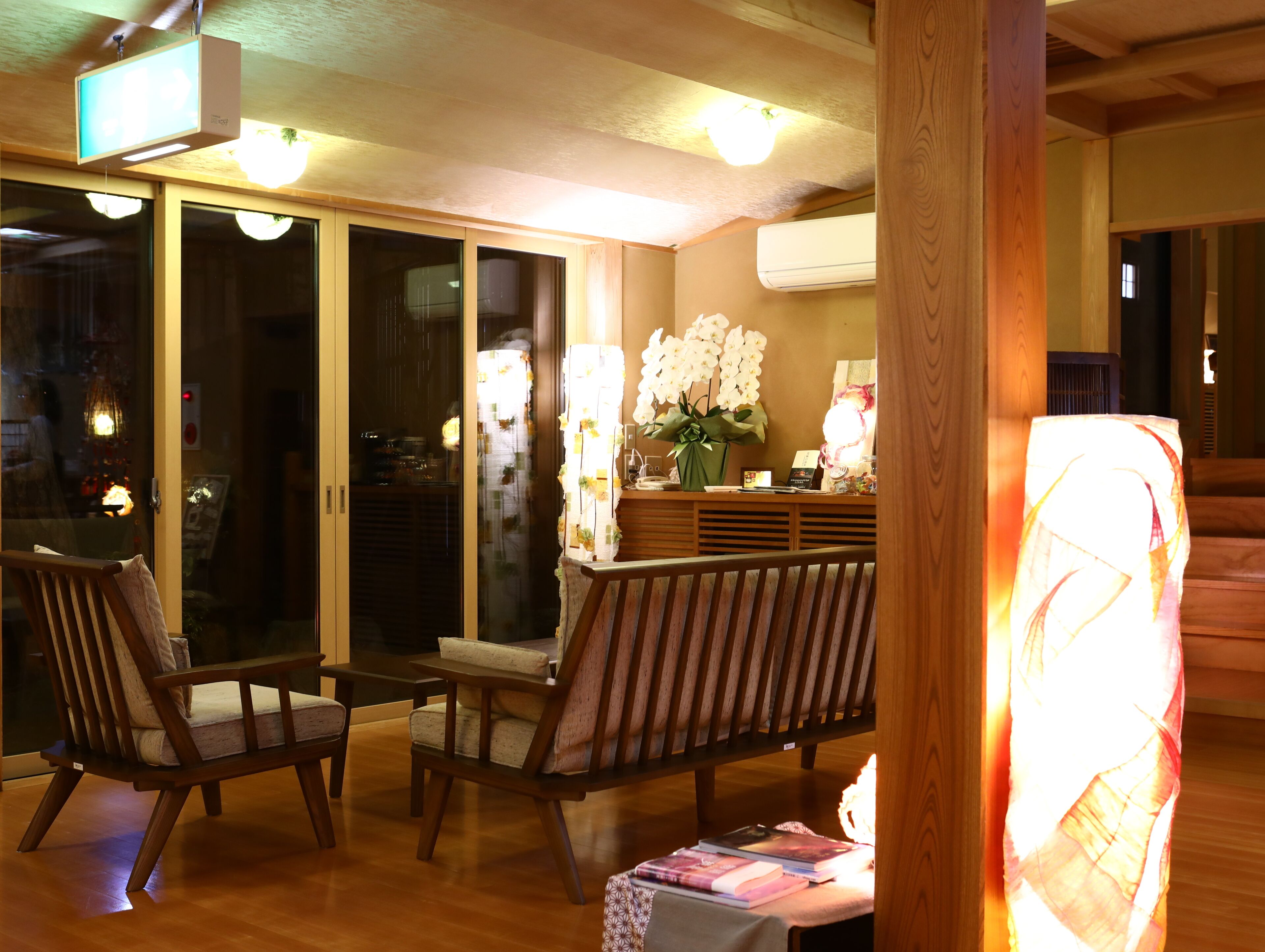 A cozy indoor seating area with wooden furniture, a reception desk with a vase of flowers, and a large window with a view outside.