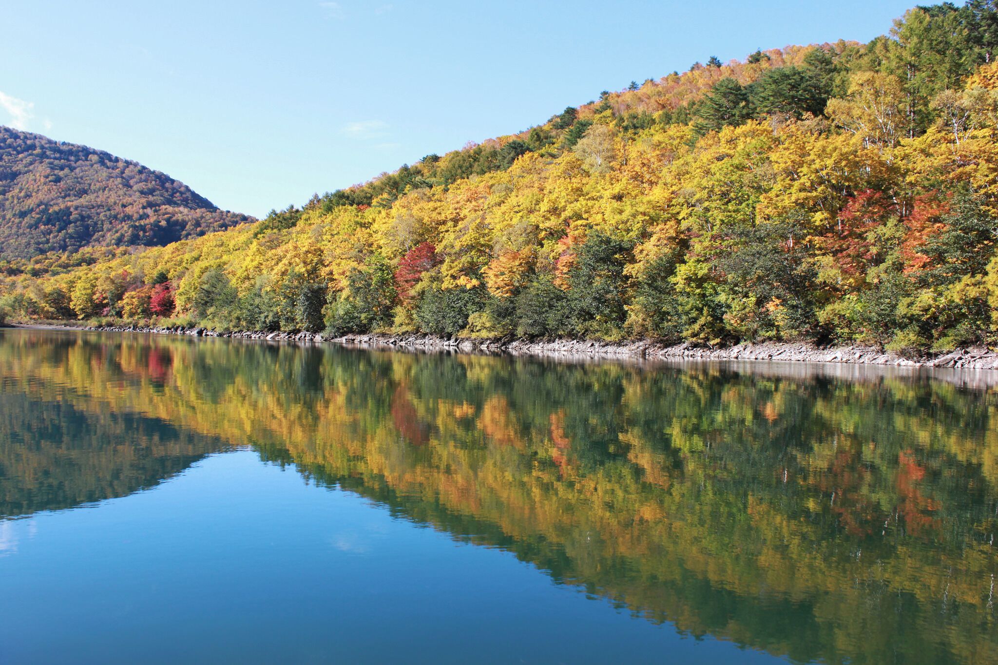 A calm lake reflecting colorful autumn trees and a mountain in the background.