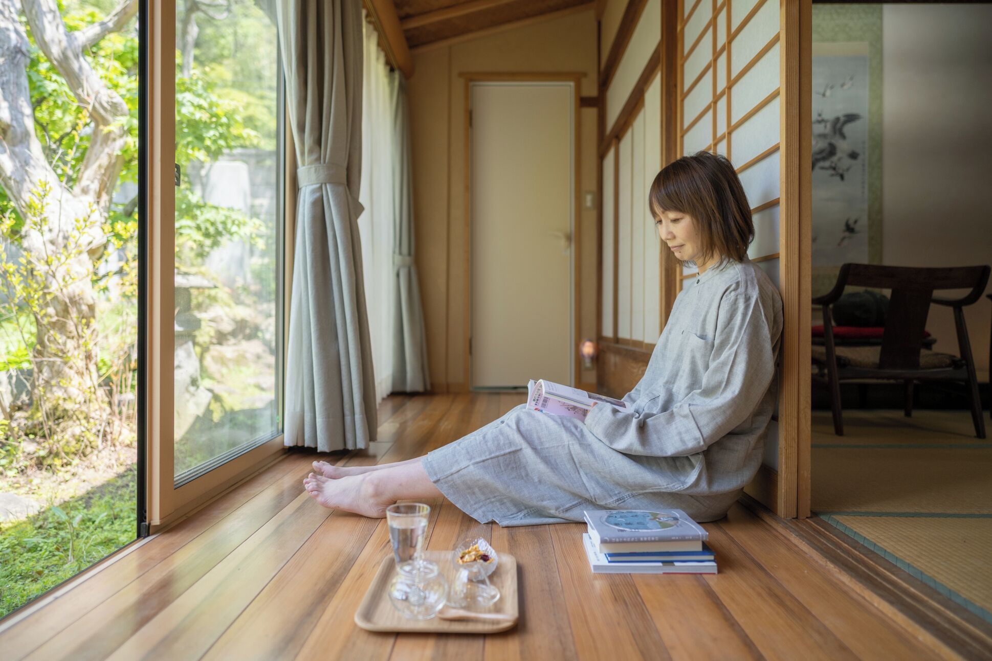 A person sitting on the floor in a room with wooden flooring, large windows, and sliding doors.