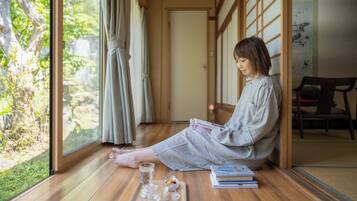 A person sitting on the floor in a room with wooden flooring, large windows, and sliding doors.