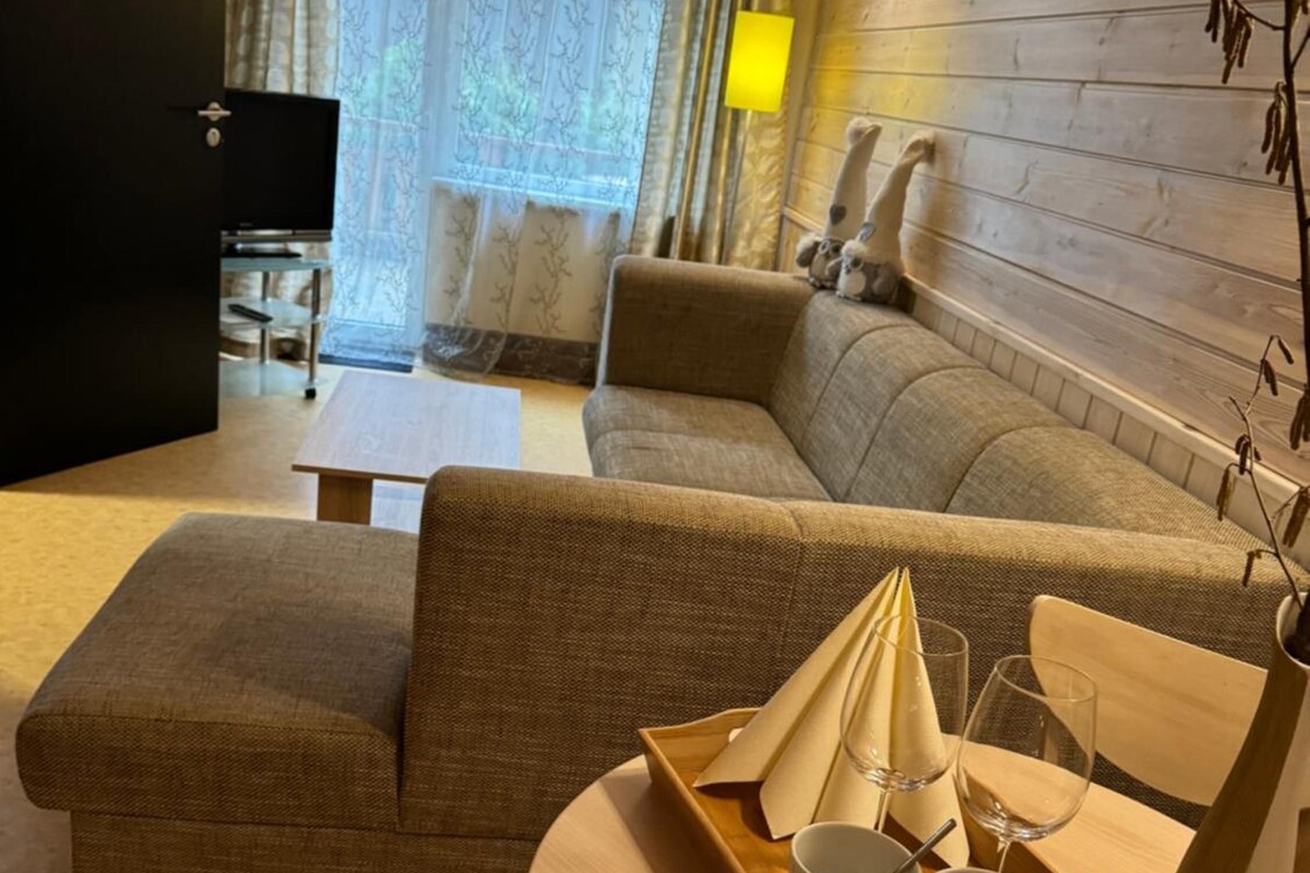 A living room with a sofa, a coffee table with a tray of cups and glasses, and a television in the background.
