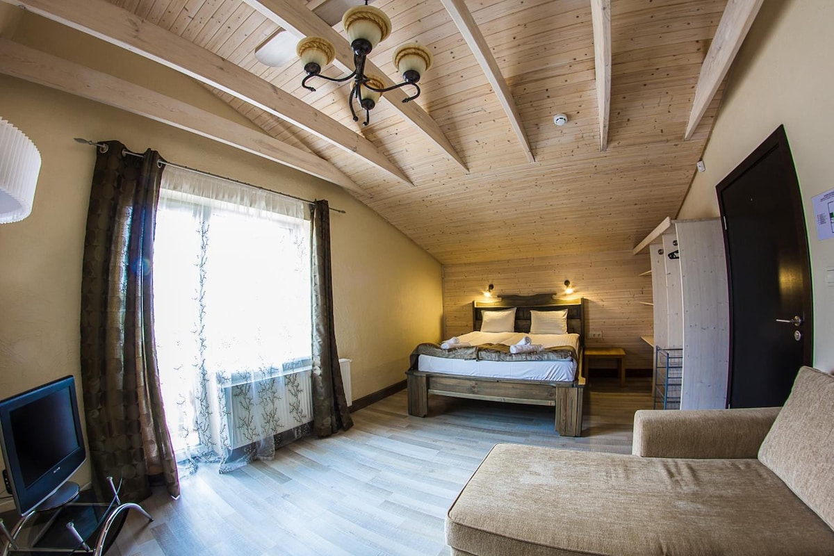 A room with a bed, a sofa, a TV, and a window with curtains.