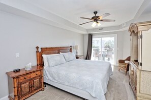 A bedroom with a large bed, wooden nightstand, and a ceiling fan.