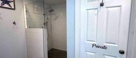 A private bathroom with a glass-enclosed shower, white tiled walls, and a wooden floor.