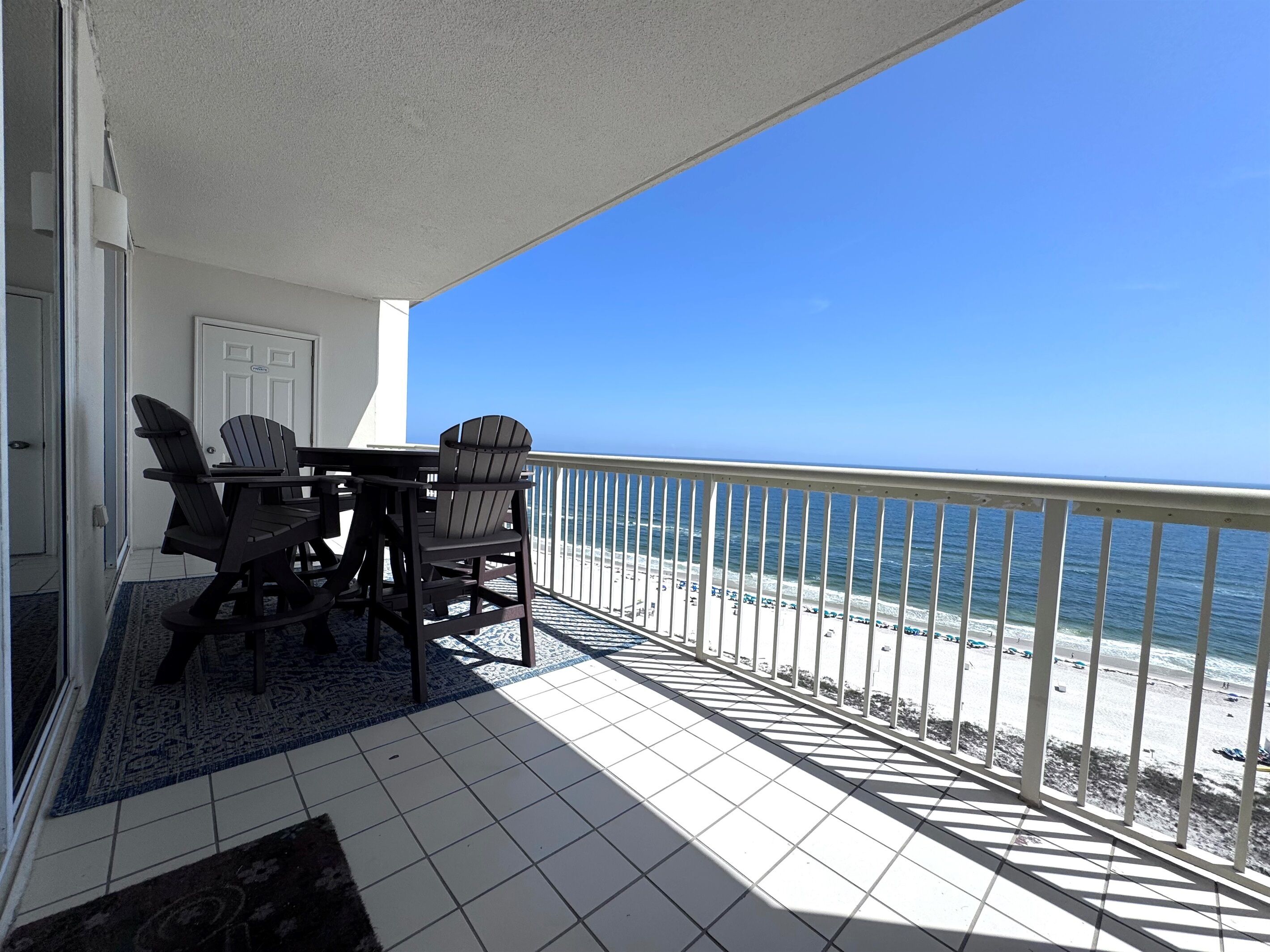 Ein Balkon mit Blick auf den Strand, einem Tisch mit Stühlen und einer Tür.