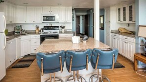 A kitchen with white cabinets, a granite countertop, a central island with bar stools, and a microwave. - Gearhart House G616 (Gearhart)