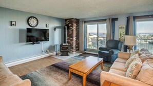 A living room with a flat-screen TV, a fireplace, a sofa, a coffee table, and a balcony with a view. - Gearhart House G616 (Gearhart)