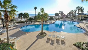 Zona de piscina con sillones de descanso y palmeras, con vista a una playa y al océano.