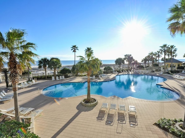 Un espace piscine agrémenté de chaises longues et de palmiers, offrant une vue sur la plage et l’océan.