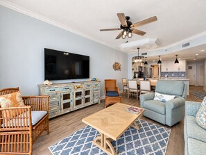 A living room with a television, a ceiling fan, a dining area, and a kitchen visible in the background. - Beach Club A1708 King/King/Queen/Sofa sleeper (Gulf Shores)