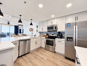 A modern kitchen with stainless steel appliances, white cabinetry, and a large island with a dishwasher. - Beach Club A1708 King/King/Queen/Sofa sleeper (Gulf Shores)