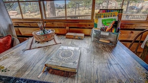 A rustic wooden table with a view of trees and a house through large windows. - Larkspur Retreat- Breathtaking Views of Longs Peak! (Estes Park)
