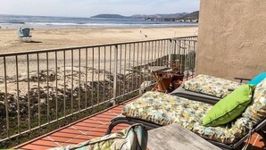 Een balkon met uitzicht op een strand en de oceaan. Er staat een stoel en een tafel met een plant in pot.