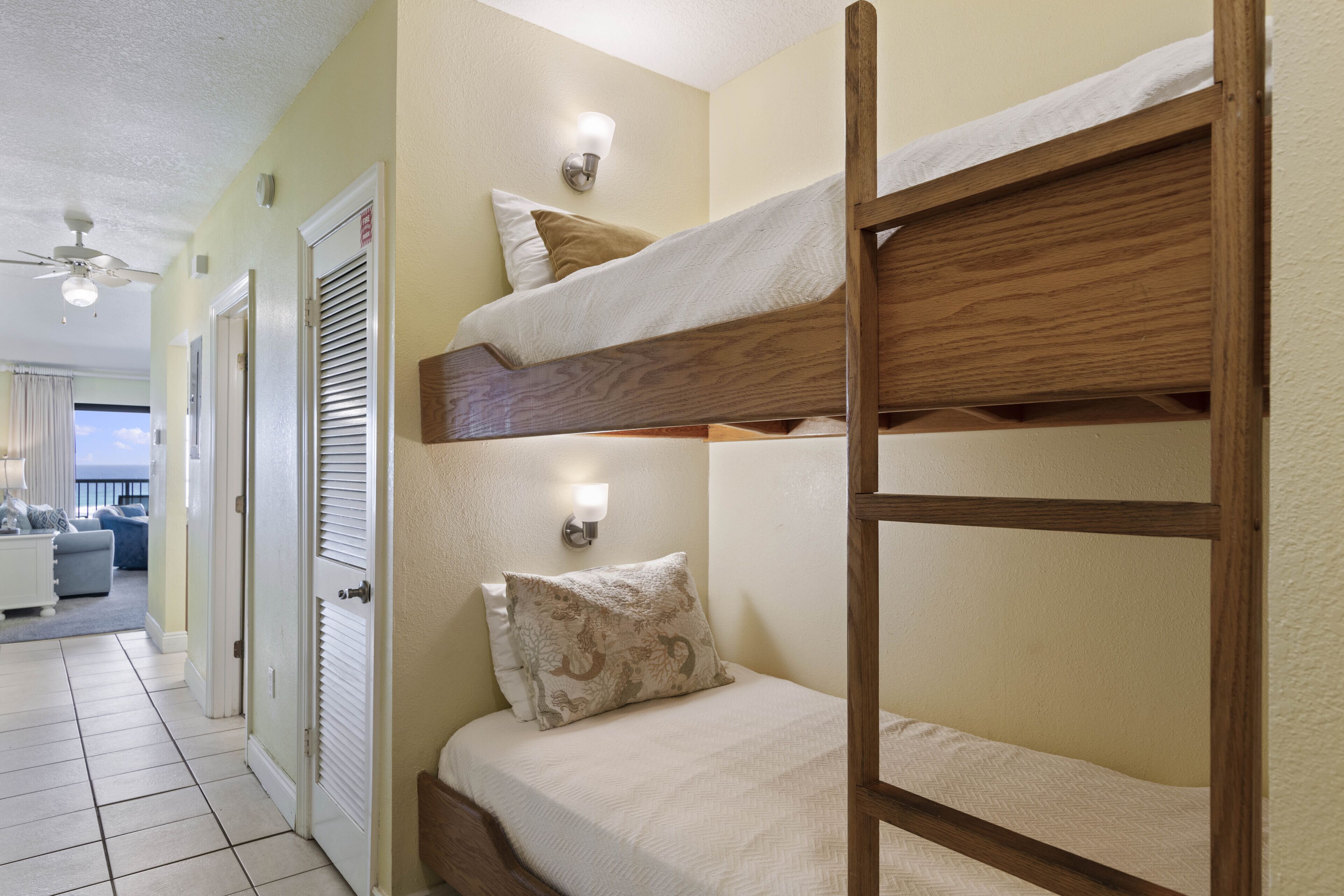 Une chambre avec un lit superposé, une échelle, une porte et un luminaire fixé au mur.