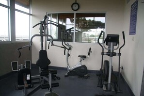 A gym with exercise equipment, a clock on the wall, and a window with a view.