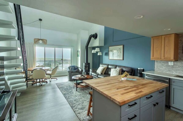 A modern kitchen with a wooden island, a dining area with a table and chairs, a living room with a sofa, and a staircase. - Gearhart House G697 (Gearhart)